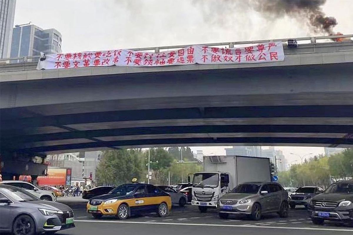 2022年10月13日，北京海淀区，四通桥上一名抗议者挂起两条横幅并点燃轮胎，吸引路人注意。（网络图片）