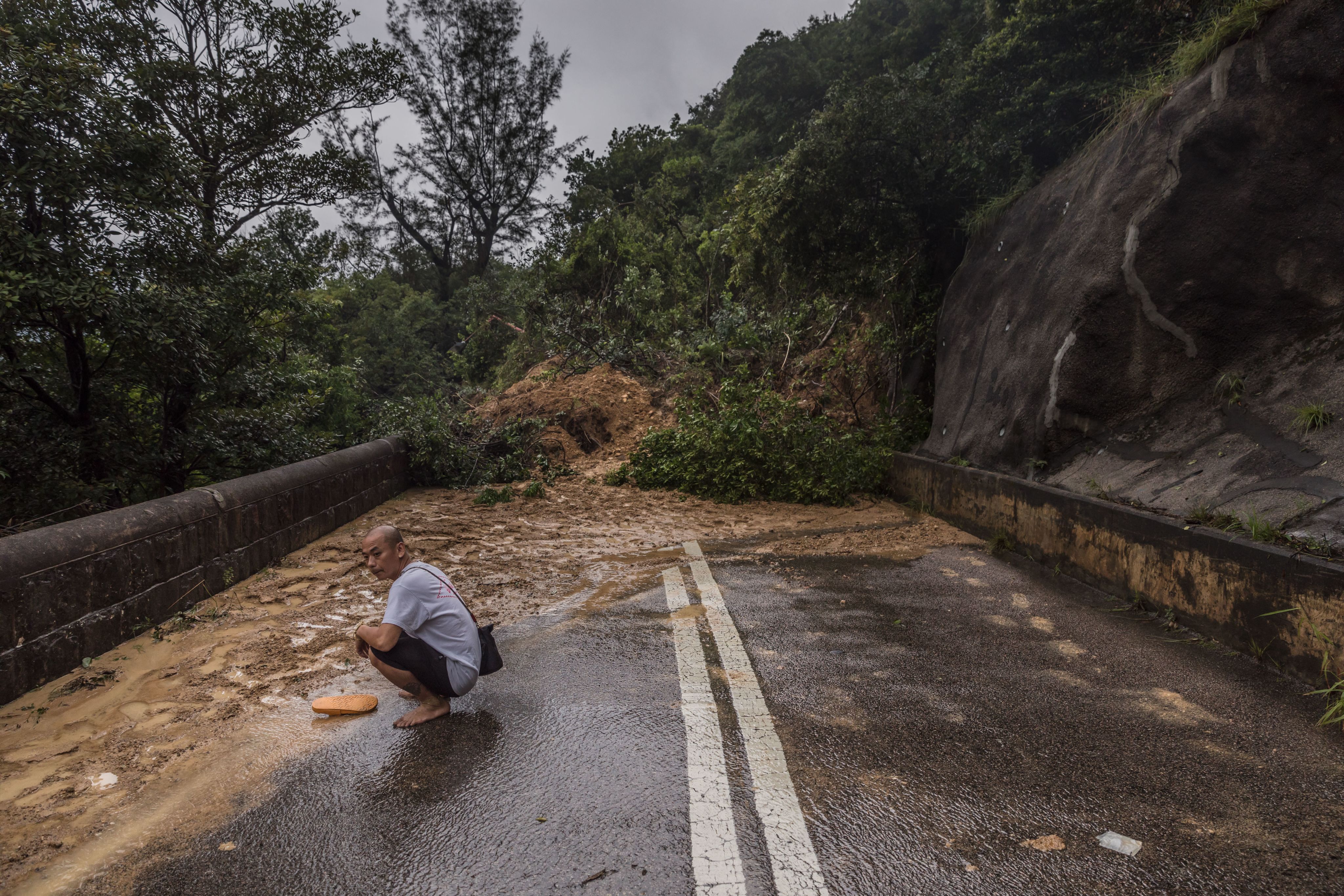 2023年9月8日，香港，一名男子蹲在一段因暴雨引发的山体滑坡区域前。(Dale DE LA REY / AFP)