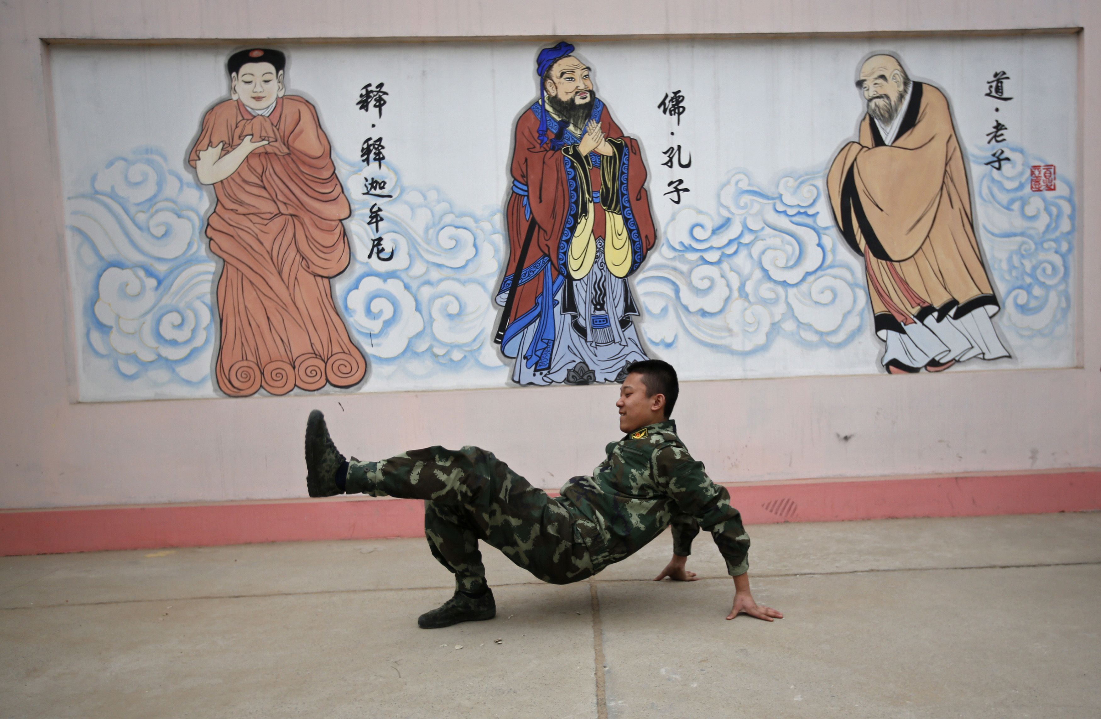 2014年2月26日，北京，某网瘾戒除中心内，一名学生身着军装在“佛祖”、“孔子”和“老子”画像前进行表演。（REUTERS / Kim Kyung-Hoon）