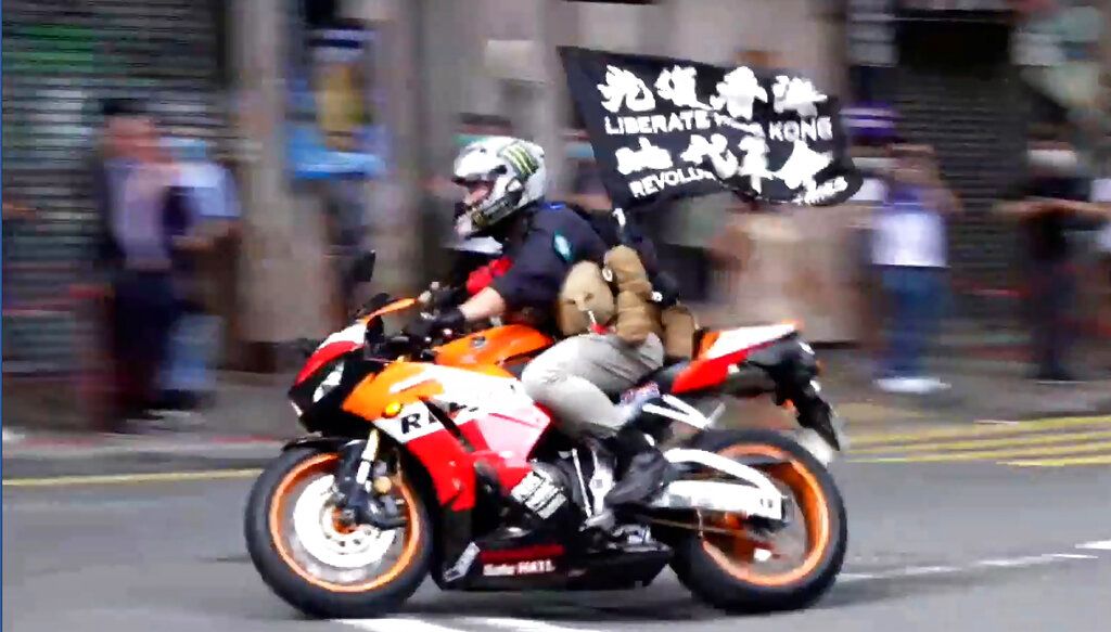 2020年7月1日，港版国安法刚刚颁布，传统七一游行首次得不到合法批准，被认定为“非法集会”。但依然有不少人走上街头。示威者唐英杰骑着挂有“光复香港，时代革命”口号的旗帜的摩托车。他被指骑着摩托冲撞警察，被逮捕并控告违反国安法，成为港版国安法第一宗案件。(AP/香港有线电视截屏)