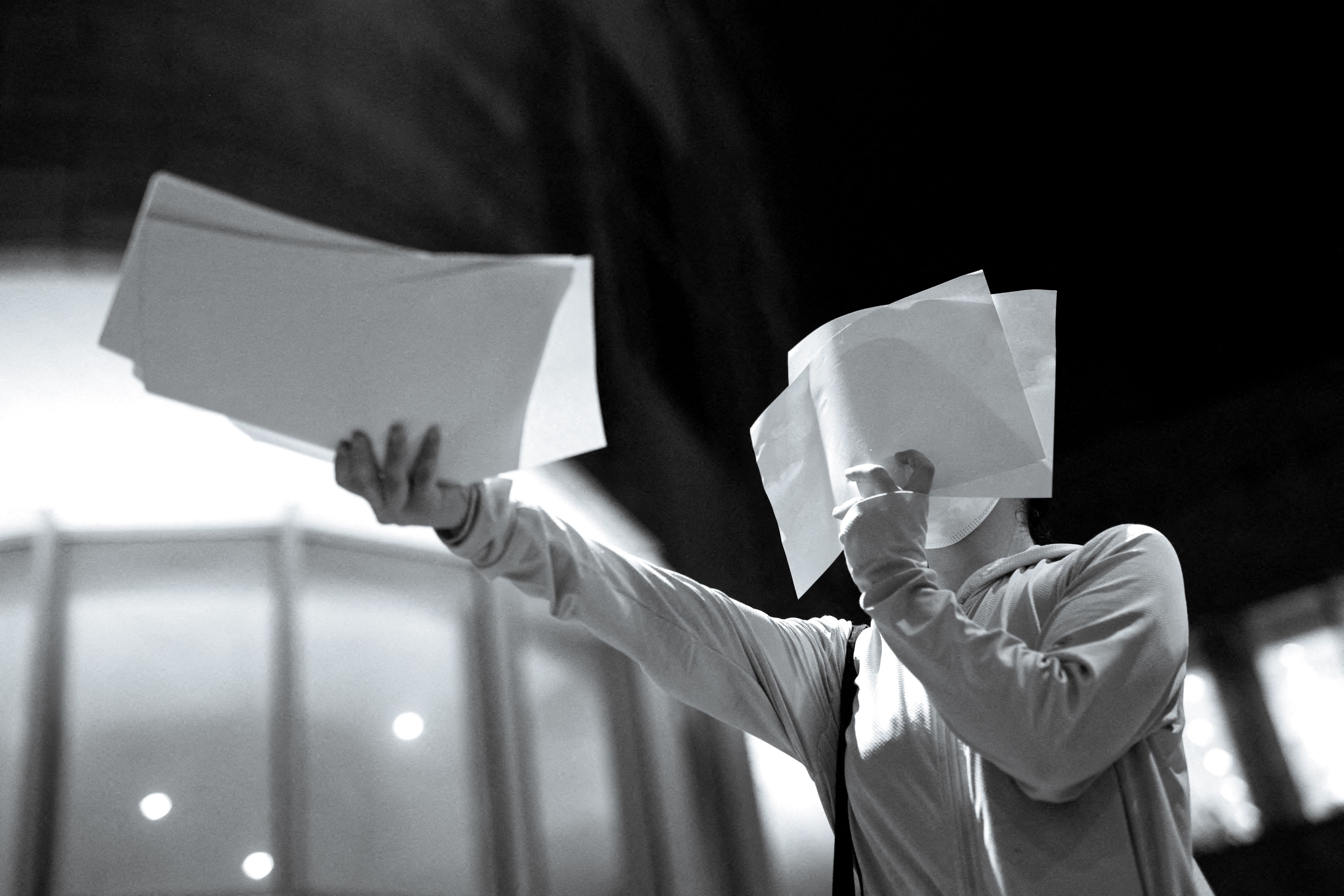 A protester distributes blank sheets of paper at a vigil for the victims of the Urumqi fire at the University of Hong Kong on November 29, 2022. (REUTERS / Tyrone Siu)