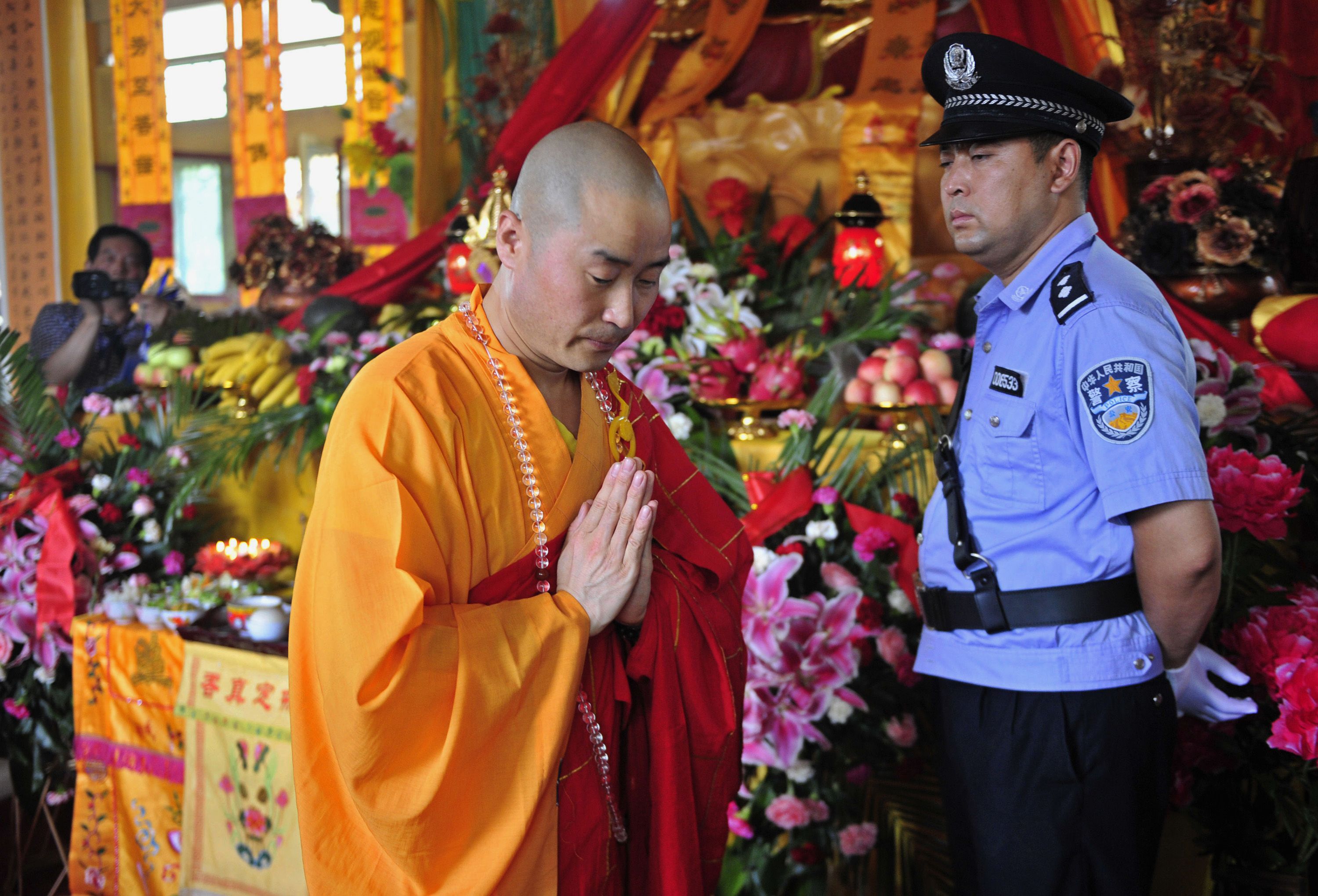陕西省白水县妙觉寺，一名僧人在警官的注视下参加为期一天的佛舍利归还仪式。