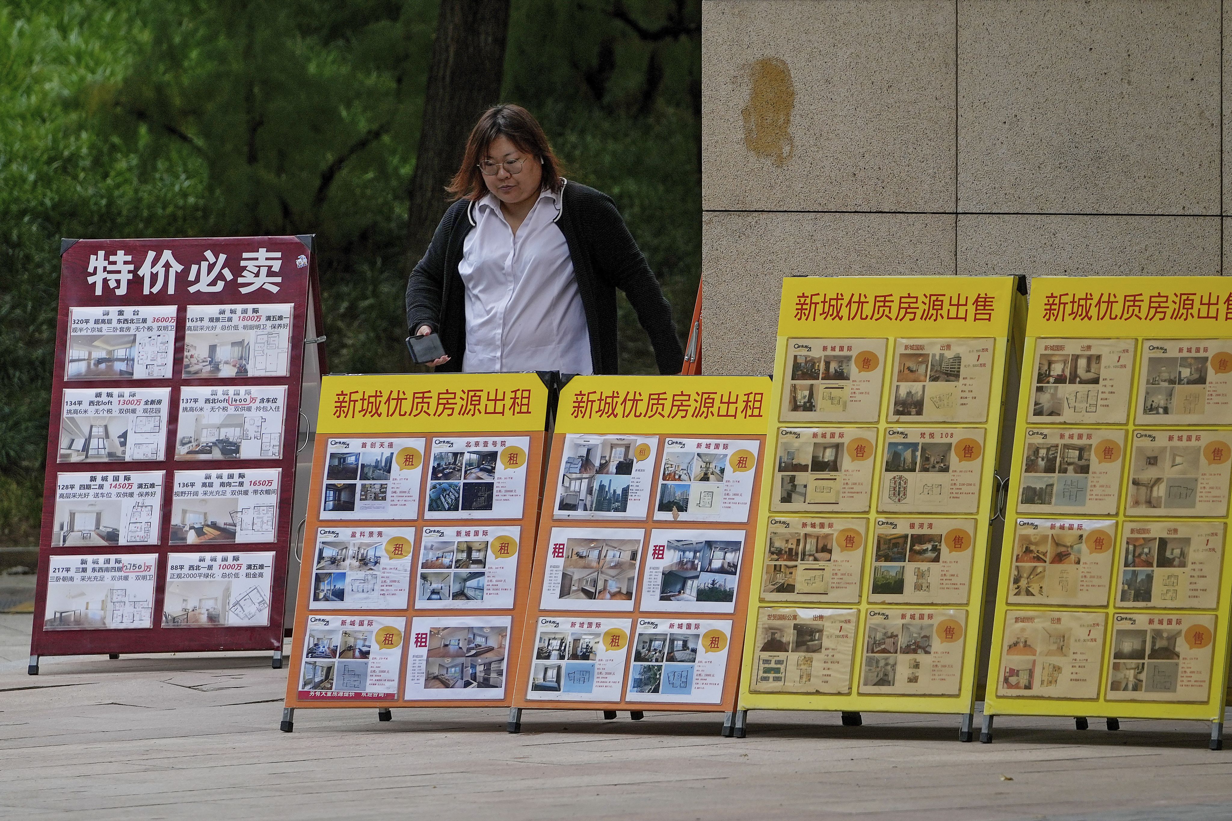2021年10月5日，一名妇女走过北京销售办公室外展示各种待售和出租房产的广告牌。（ AP /Andy Wong）