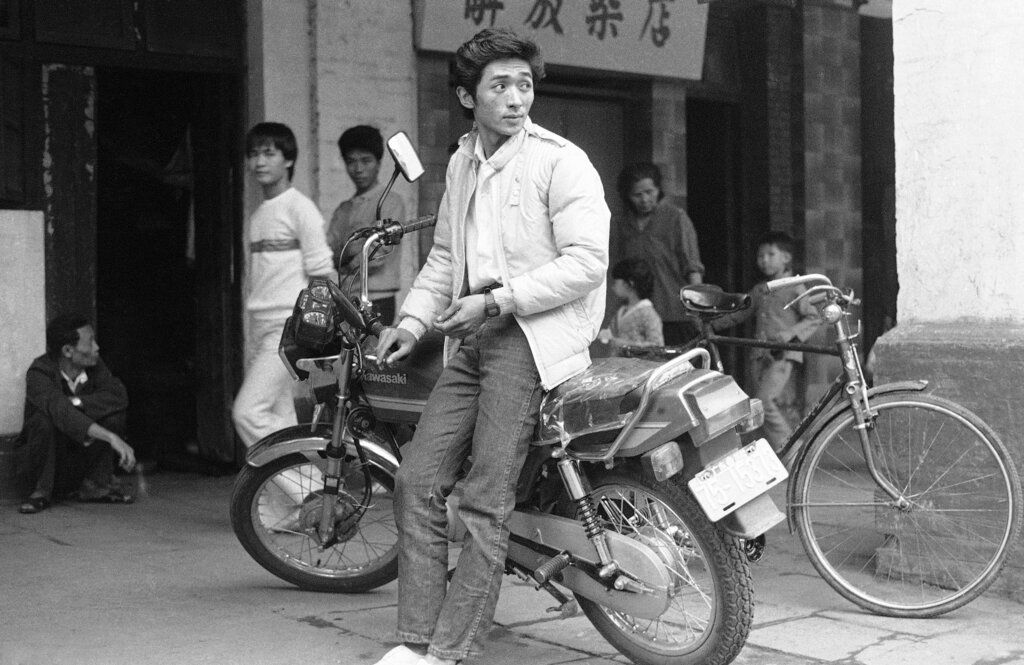 1984年11月27日，广东省，街头一名身穿牛仔裤的男青年倚靠在日本产的“川崎”摩托车上。(AP Photo/Rick Gladstone)