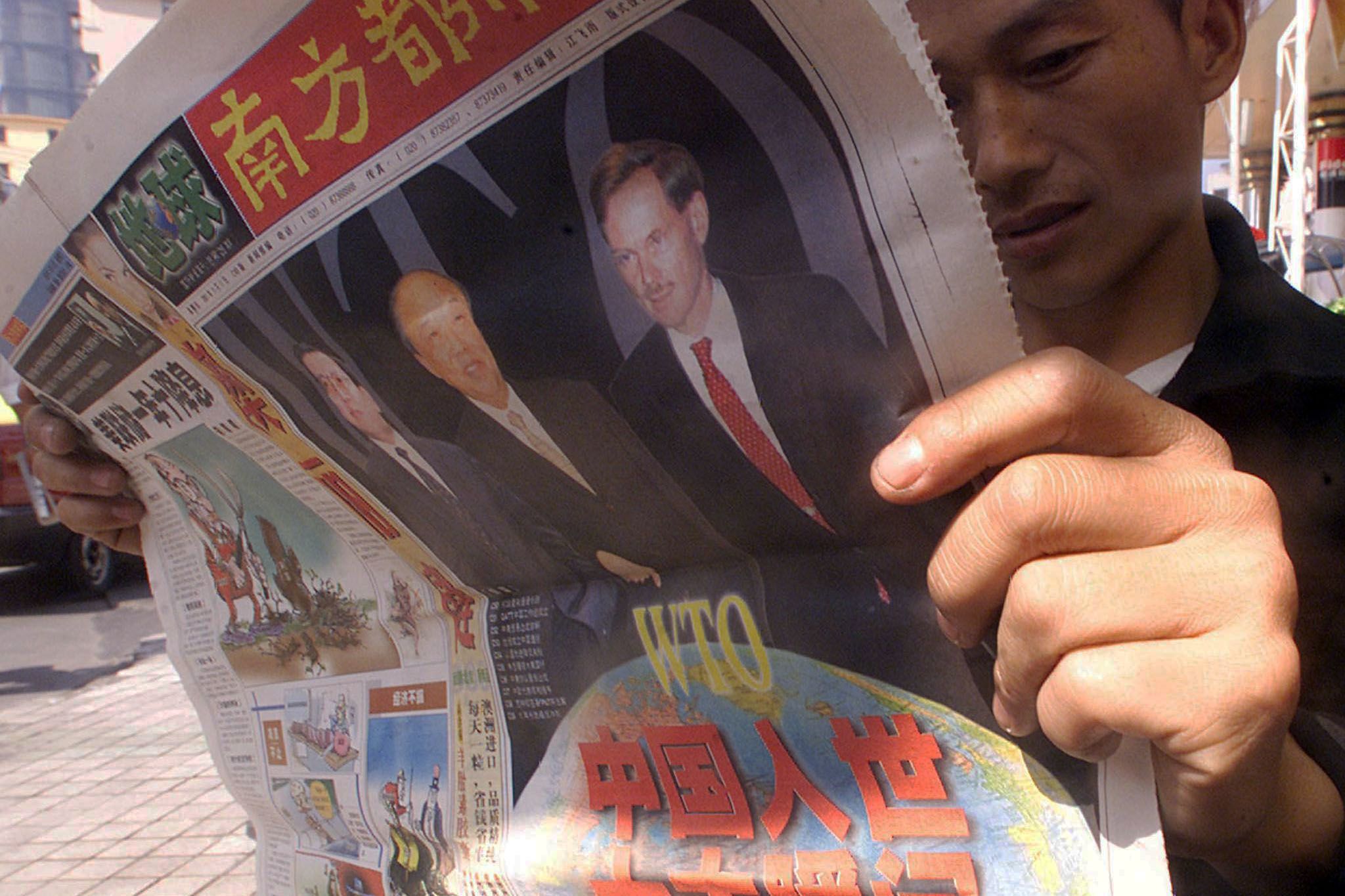 2001年11月11日，广东省广州市，一名男子在街道上阅读有关中国加入世界贸易组织 (WTO) 的报纸。在前一日，中国在卡塔尔首都多哈举行的 WTO 会议上正式被批准加入 WTO。（AFP / Peter PARKS）