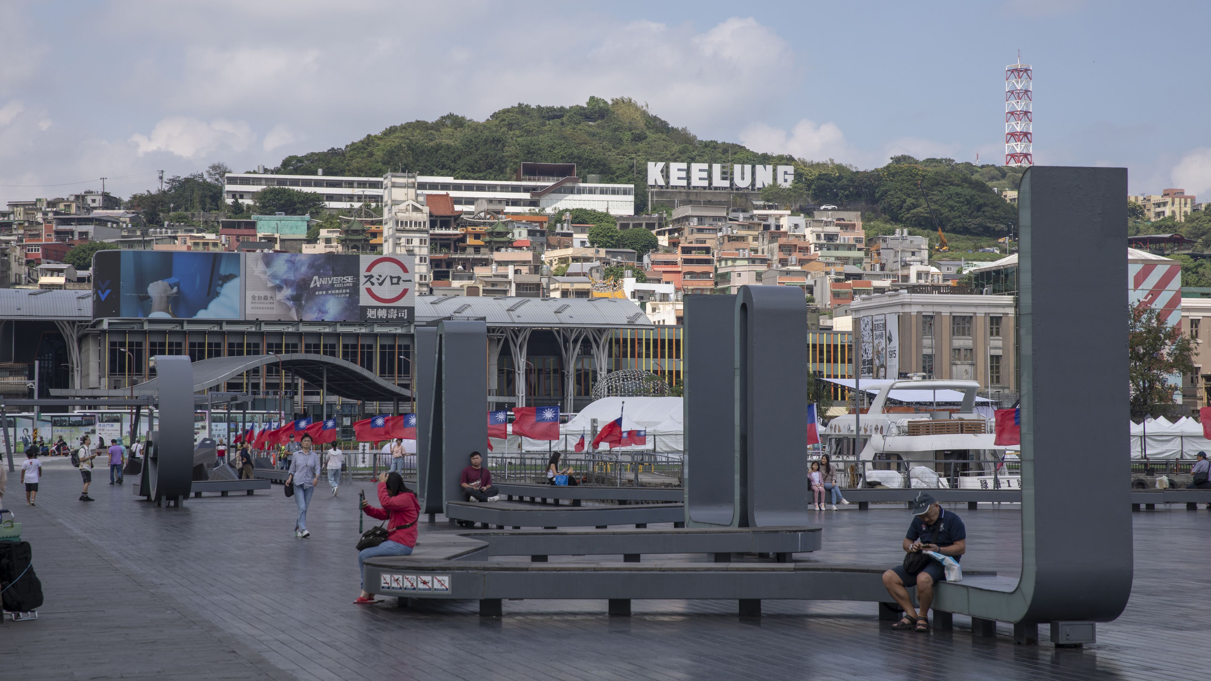 市民在基隆海洋广场边休息，身后是太平山上著的“KEELUNG”标牌。曾经太平山上主要是附近打渔的渔民居住，如今已经成为基隆最著名的景观。