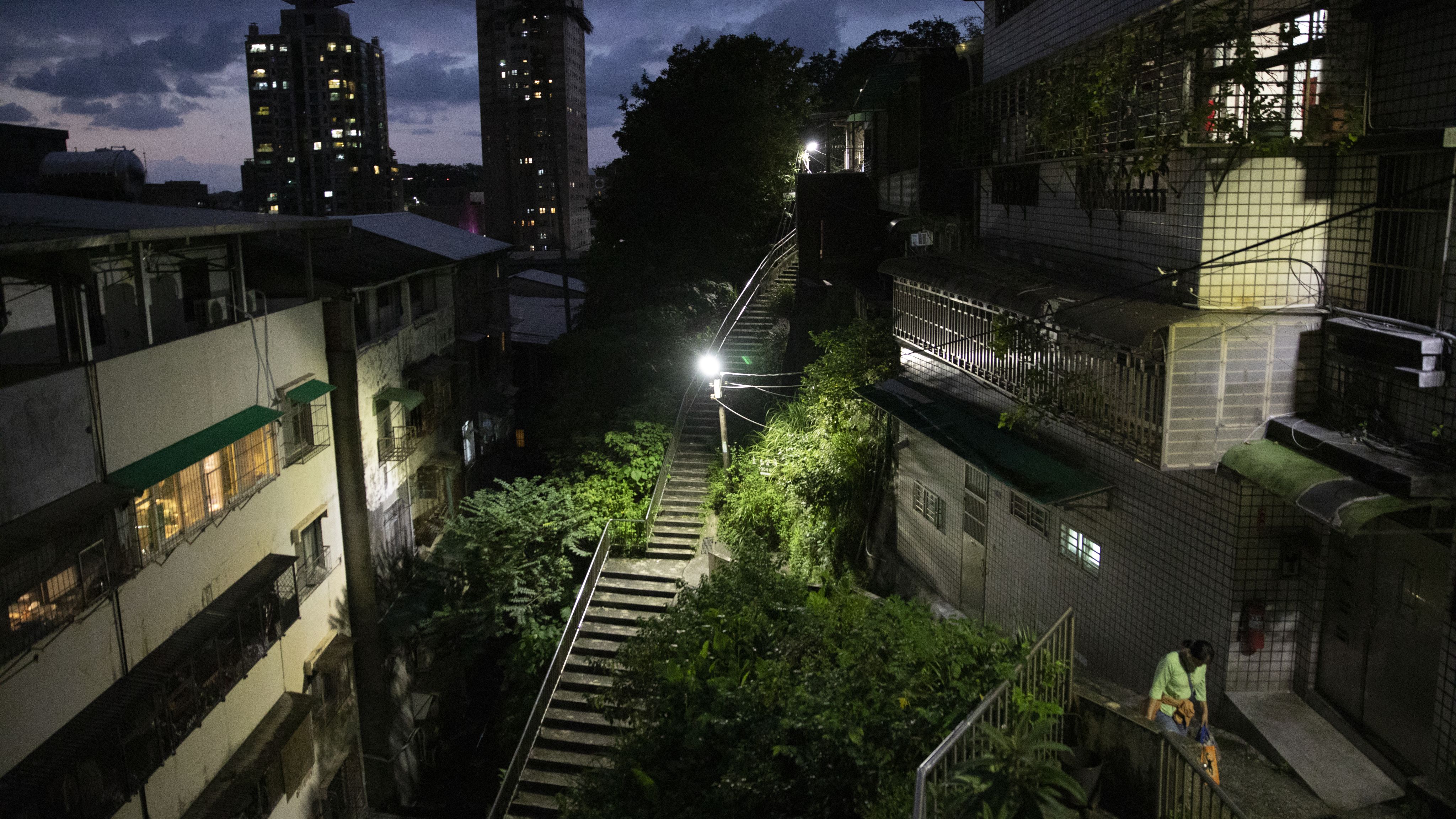 基隆市区周边山坡上，一名女子在夜色下走过民宅。