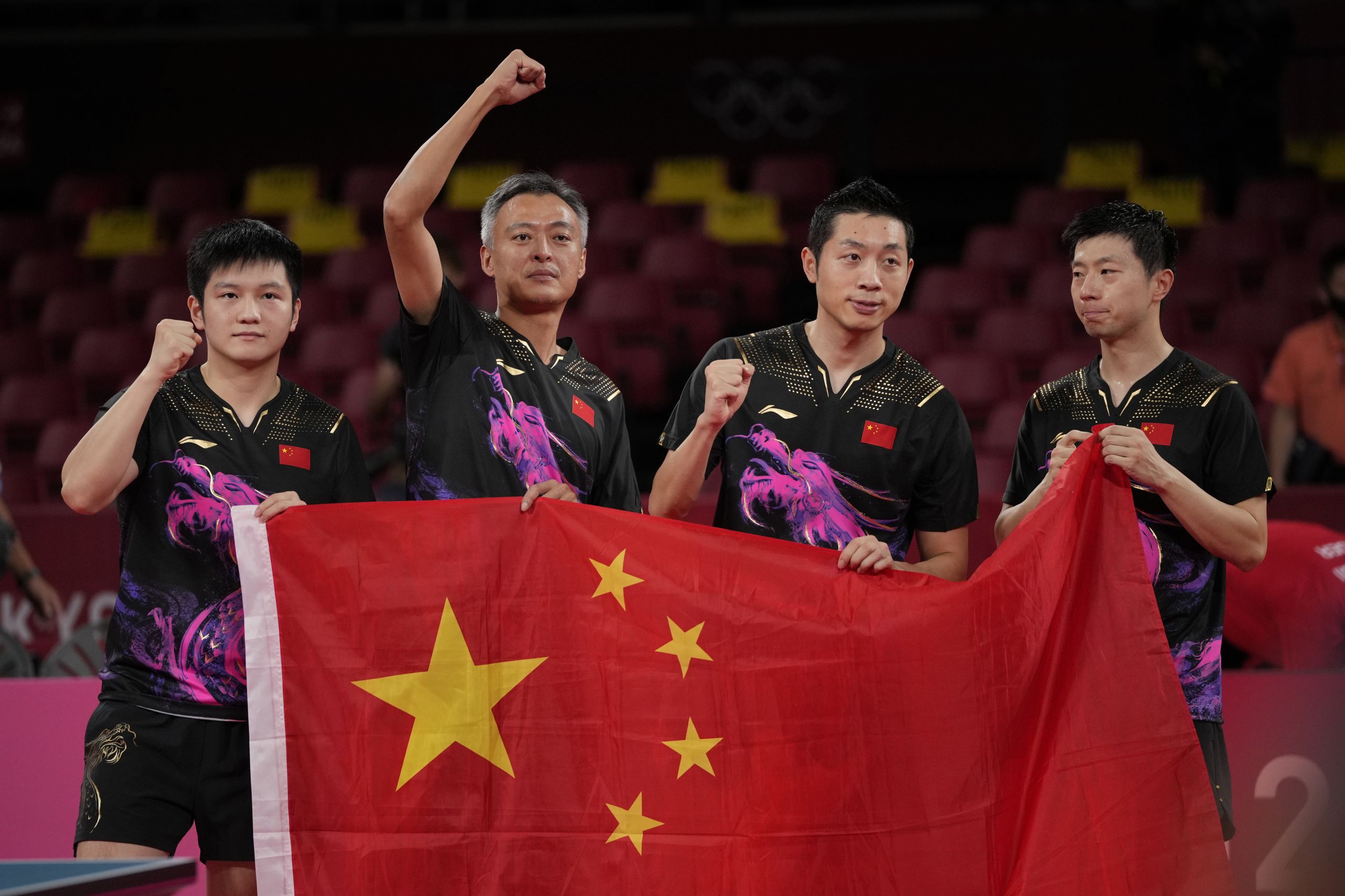 乒乓球男子团体金牌比赛中，中国队的范振东、教练秦志健、许昕和马龙在击败德国队后与中国国旗合影。