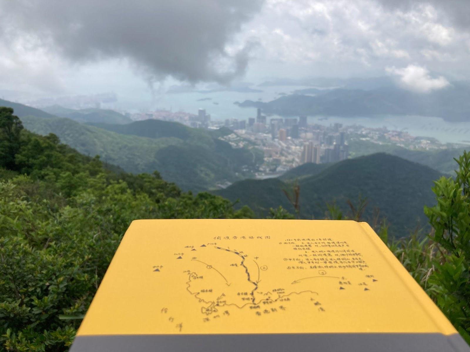 黄铠带着《大逃港》这本书爬上梧桐山，对面是香港，《大逃港》的背面印着梧桐山的逃港路线。