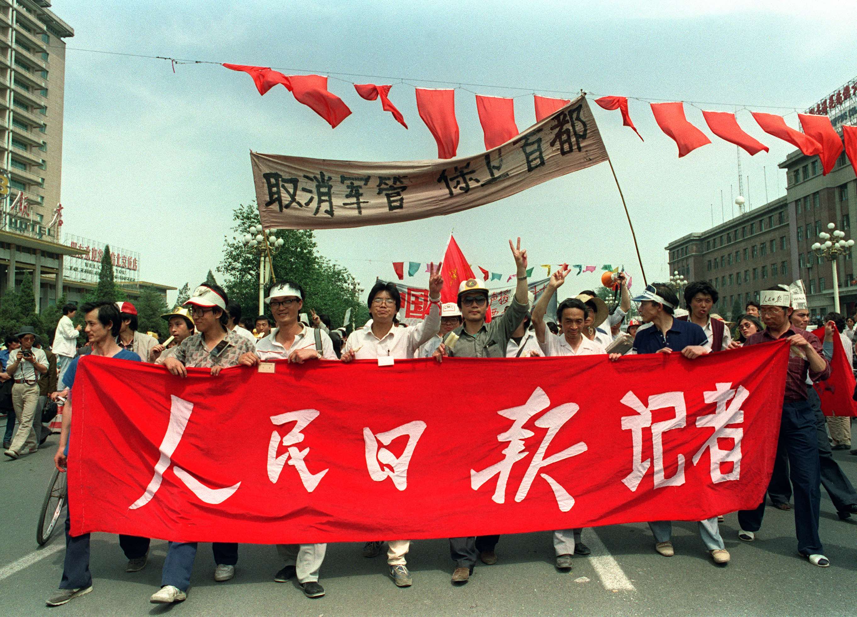 1989年5月22日，官方报纸《人民日报》的记者举着“取消军管，保卫首都”的横幅，带领游行队伍向天安门广场游行，以支持支持民主的学生。